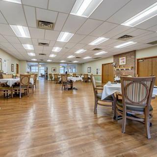 An empty dining room with wooden floors and neatly arranged tables and chairs.