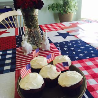Patriotic cupcakes adorned with American flags on a red, white, and blue table setting.