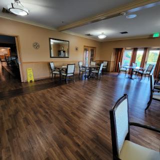 A spacious and well-lit dining area with wooden flooring, featuring tables and chairs arranged for guests.