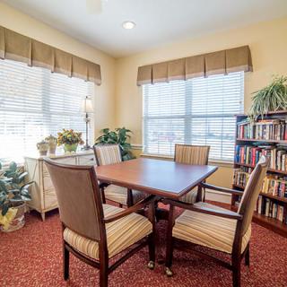 A cozy meeting room with a wooden table, chairs, large windows, and bookshelves.