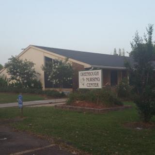 A building with a sign in front, surrounded by greenery during the evening.