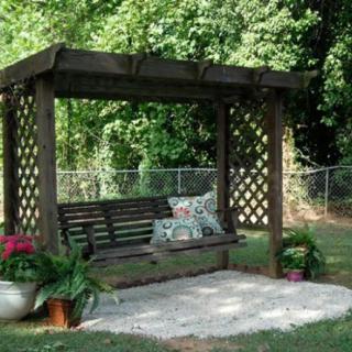 A wooden pergola with a swing is set in a garden, surrounded by potted plants.