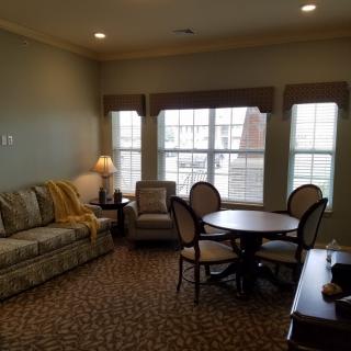 A cozy living room with a sofa, armchair, and a round table surrounded by chairs near large windows.
