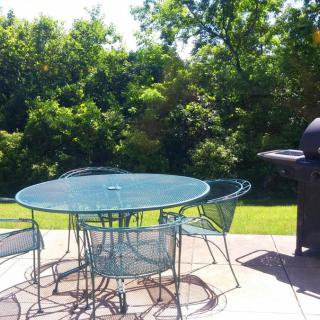 A sunny backyard patio with a table, chairs, and a grill.
