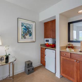 A compact kitchenette with wooden cabinetry, featuring a microwave, refrigerator, and decorative elements.