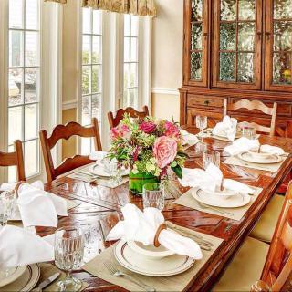 A beautifully set dining table in a bright, elegant room with wooden furniture and floral centerpiece.