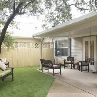 A peaceful backyard patio with comfortable seating, a lush lawn, and shade from a large tree.
