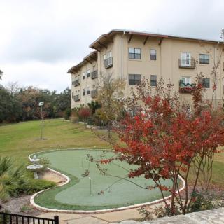 A view of an apartment building with a landscaped lawn and trees in autumn colors under an overcast sky.