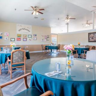 Spacious dining room with round tables, decorated with flowers and ceiling fans overhead.