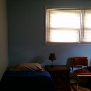 A minimalist bedroom with a bed, nightstand, lamp, and chair by the window.