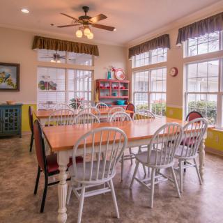 A bright and spacious dining room with a large table surrounded by chairs and multiple windows.