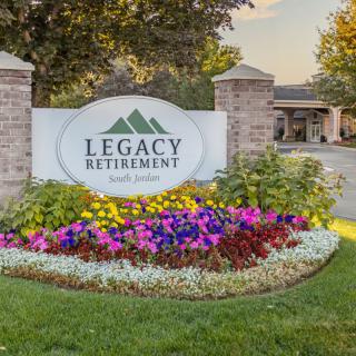Entrance sign of Legacy Retirement community with vibrant flowers and landscaping.