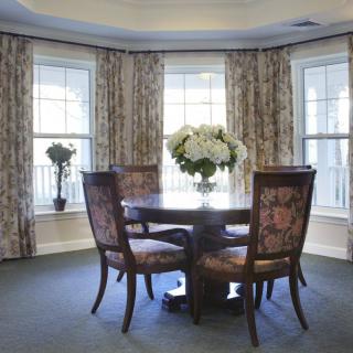 A cozy dining area with a round table and chairs, surrounded by large windows and elegant curtains.
