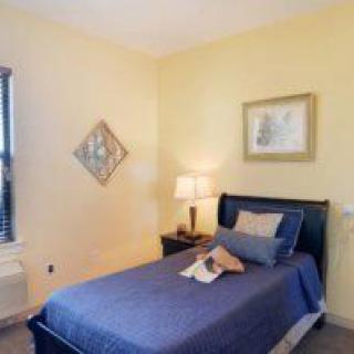 A cozy bedroom with a neatly made bed, a lamp on the nightstand, and framed artwork on the walls.