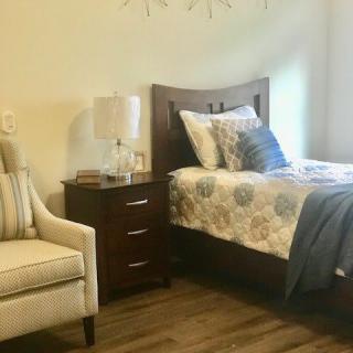 A cozy bedroom with a neatly made bed, nightstand, and armchair.