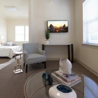 A modern and cozy living room with natural light, featuring a chair, a wall-mounted television, and stylish decor.
