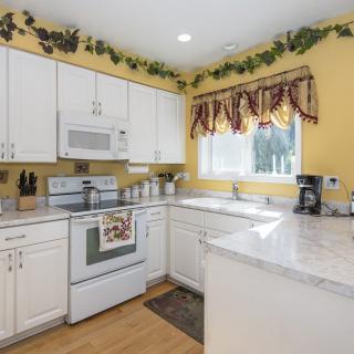 A cozy kitchen with white cabinets, yellow walls, and decorative vine accents.
