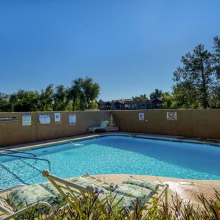 An outdoor swimming pool surrounded by a fence with trees in the background under a clear blue sky.