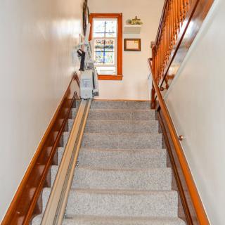 A staircase equipped with a stair lift for accessibility, featuring carpeted steps and wooden handrails.