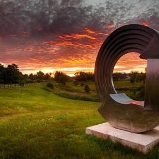 A stunning metal sculpture set against a vibrant sunset, creating a beautiful contrast with the lush green landscape.