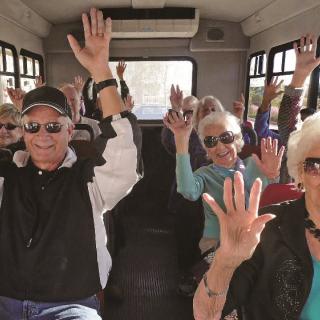 A group of seniors enjoying a lively bus ride, raising their hands in excitement.