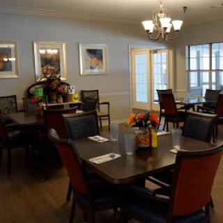 A well-lit dining room with neatly arranged tables and chairs, decorated with flowers and artwork.