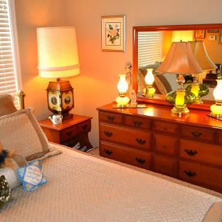 A cozy bedroom with vintage decor featuring a dresser, mirror, and warm lighting.