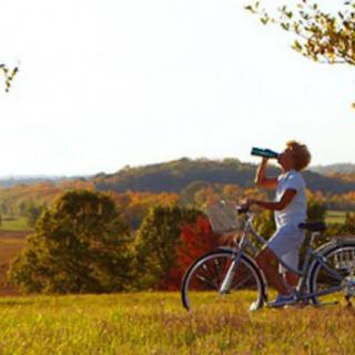 A person taking a break from cycling to enjoy the scenic landscape and have a drink during sunset.