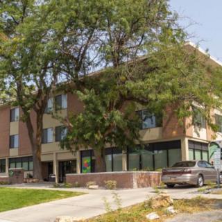 A three-story brick building with trees and a parked car in front.