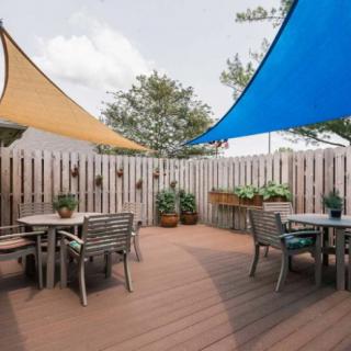 An inviting outdoor patio with shade sails, tables, chairs, and potted plants.