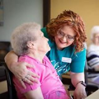 A caretaker warmly embraces an elderly woman, showing compassion and support in a nursing home setting.