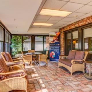 A cozy indoor seating area featuring wicker furniture and a brick floor, illuminated by natural light coming through large windows.