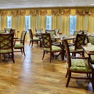 An elegant dining room with neatly arranged tables and chairs, featuring wooden flooring and decorative curtains.