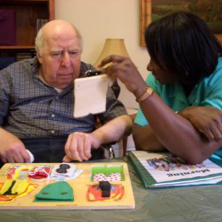 A caregiver assisting an elderly man with an activity at a nursing home.