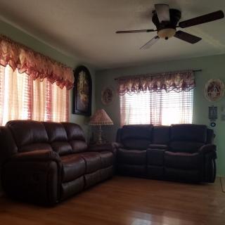 A cozy living room with leather sofas, a ceiling fan, and windows adorned with curtains.