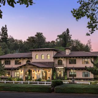 A large, elegant house surrounded by trees in the evening light.