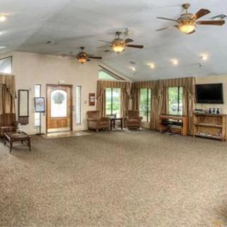 A spacious and well-lit interior with carpeted flooring, featuring multiple ceiling fans, comfortable seating, large windows, and a television.