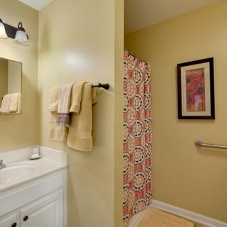 A well-lit bathroom featuring a shower with a patterned curtain, a sink with towels, and modern wall art.