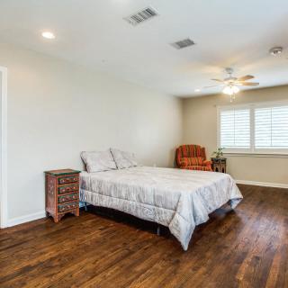 A spacious bedroom with a bed, armchair, and ceiling fan, featuring hardwood floors.