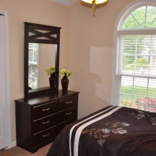 A cozy bedroom with a dark dresser, mirror, and large window.