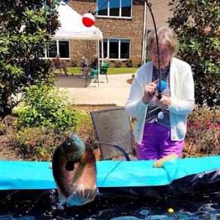 A woman enjoys a day of fishing at a pond, capturing the moment as a fish jumps out of the water.