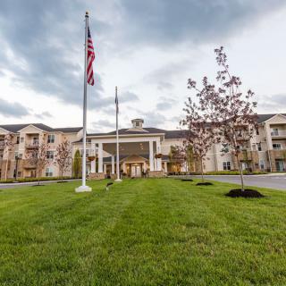 A large building with flags at the entrance, surrounded by a well-maintained lawn and trees under a cloudy sky.