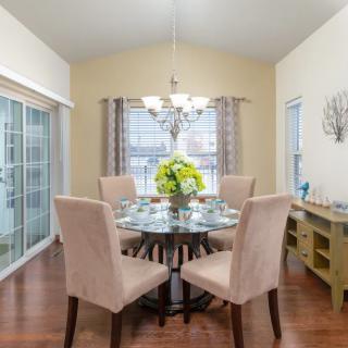 A cozy dining room with a round glass table and upholstered chairs, highlighted by a chandelier and elegant decor.
