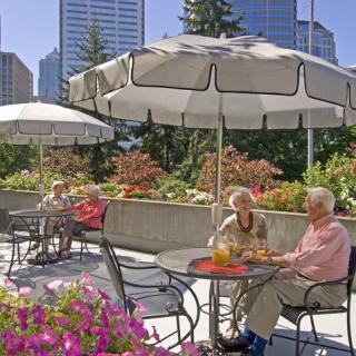 Elderly individuals enjoying a sunny day on a patio with city buildings in the background.