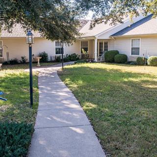 A pathway leading to a residential house surrounded by a well-maintained lawn and trees.