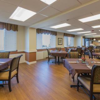 A spacious dining area with neatly arranged tables and chairs, featuring warm lighting and a wooden floor.