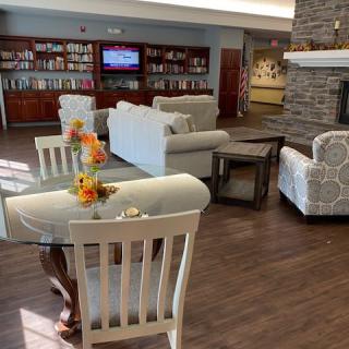 A cozy living room with sofas, chairs, and bookshelves, featuring a fireplace and floral decorations.