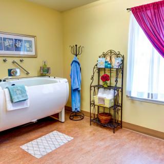 A cozy bathroom with a freestanding bathtub, bright yellow walls, and neatly arranged towels on a metal shelf.