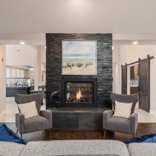 A modern living room with a central fireplace, flanked by two armchairs and decorated with a painting above.