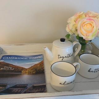 A cozy setup with a teapot, two mugs, a magazine, and flowers on a tray.
